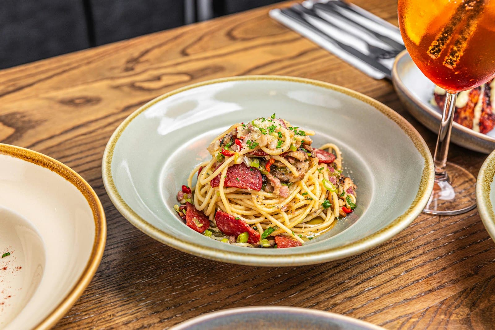 Spaghetti al guanciale piccante impiattati su un tavolo in legno, con un calice sullo sfondo