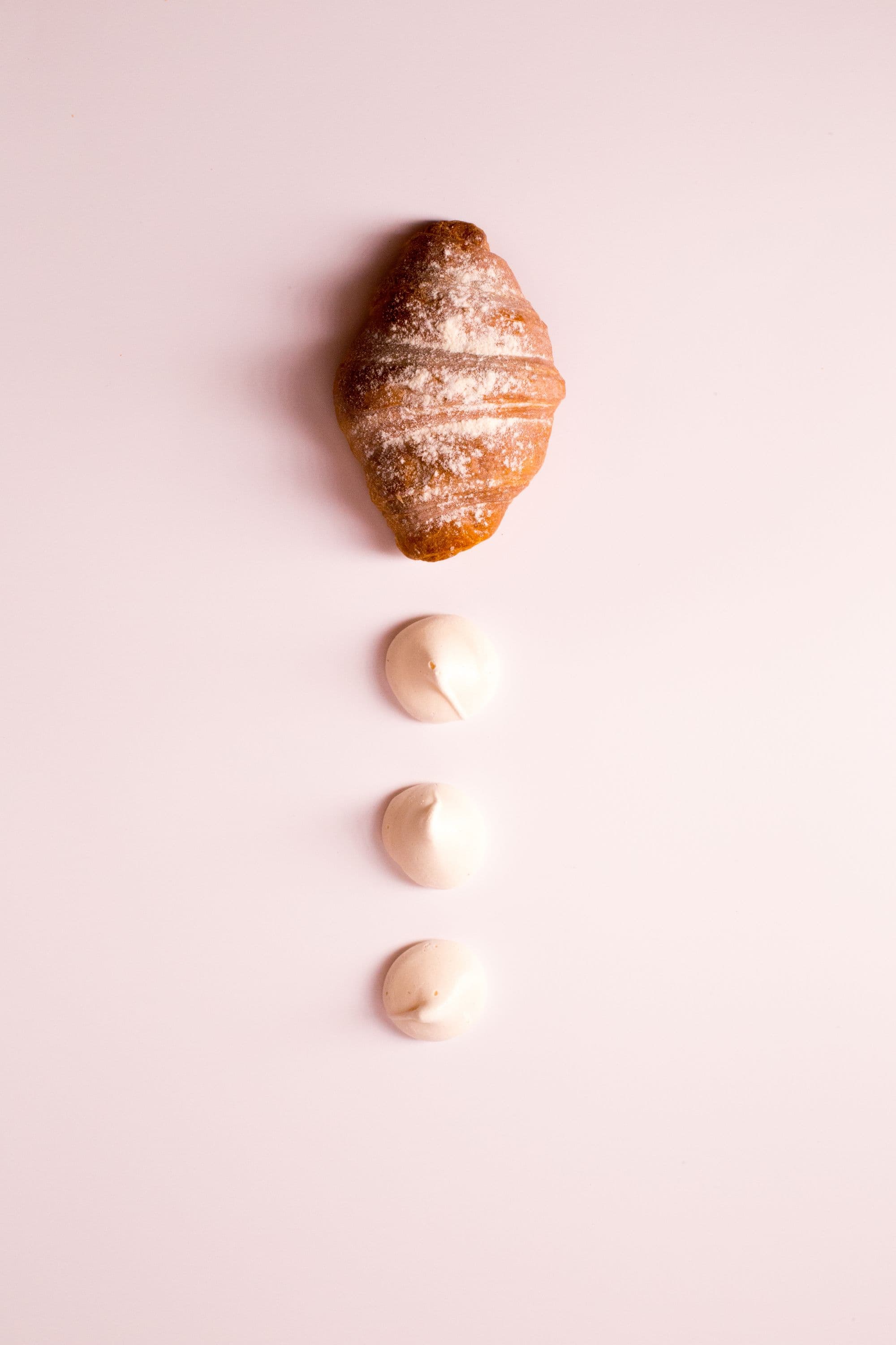 Cornetto spolverato di zucchero a velo su sfondo rosa tenue, con tre ciuffi di crema accanto