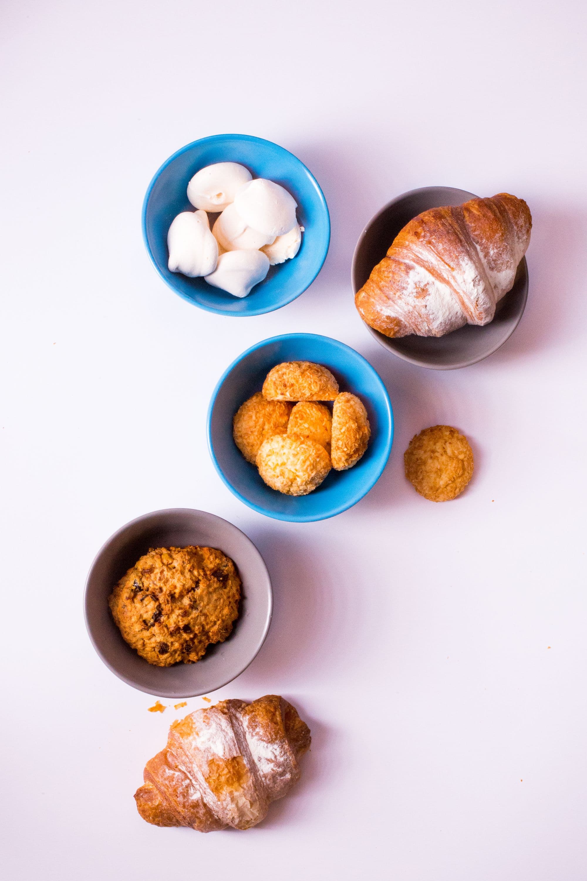 Composizione dall'alto con cornetto, meringhe, biscotti al cocco e un biscotto ai cereali in ciotoline colorate
