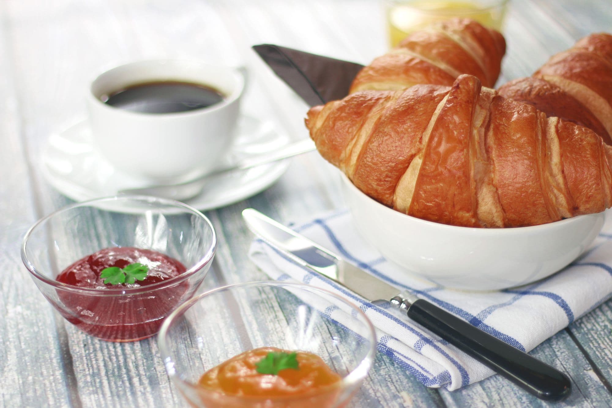 Tavolo da colazione con cornetti in una ciotola, caffè, marmellata e succo d'arancia alla luce del mattino