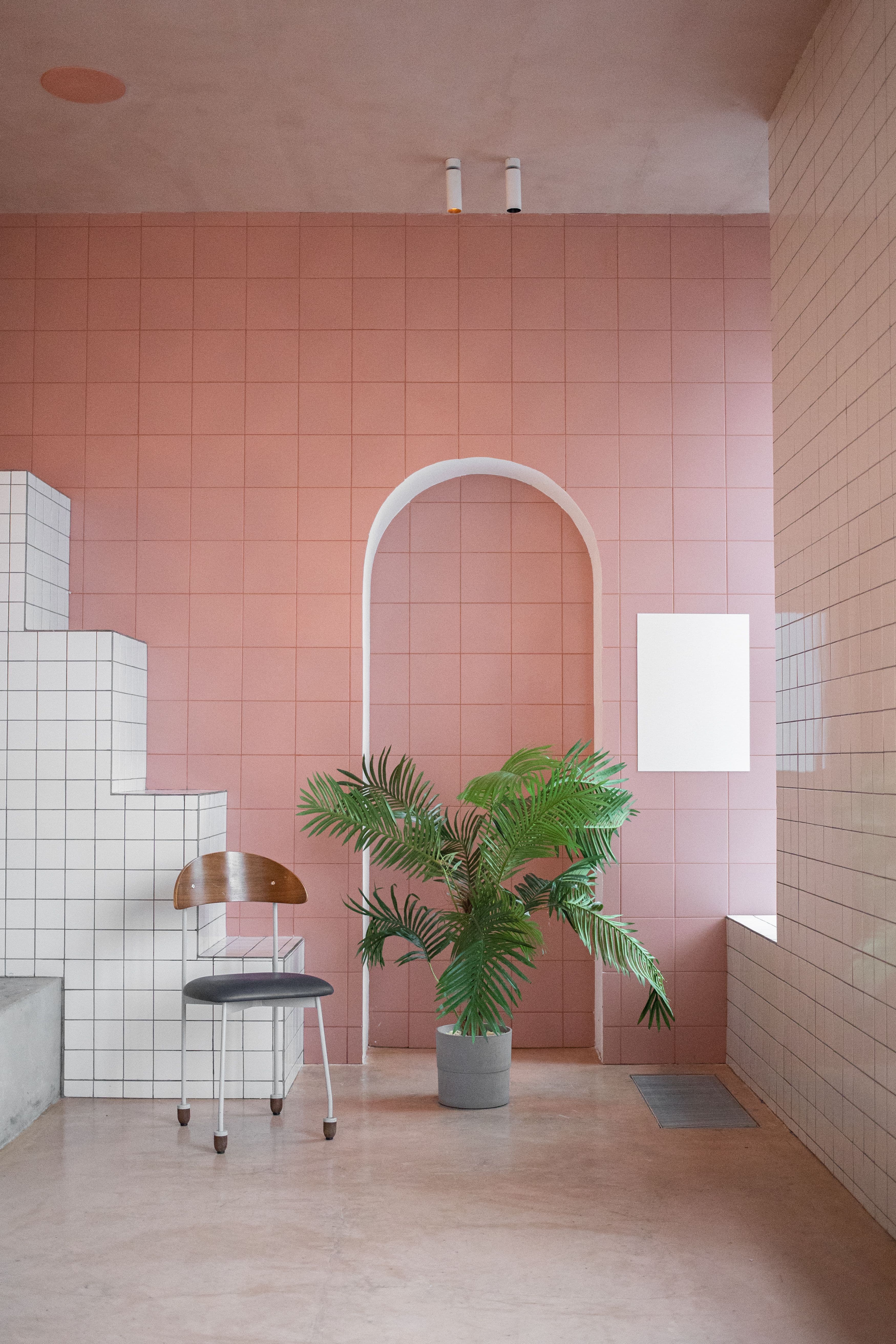 Interno elegante e minimale con pareti piastrellate rosa, arco in muratura e pianta verde