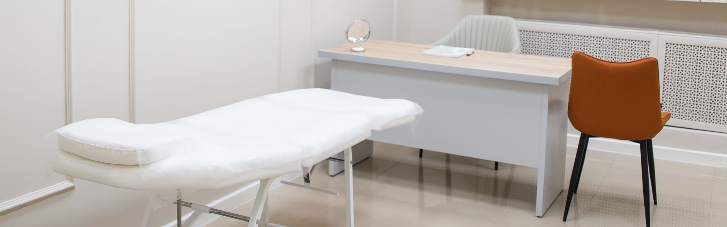 Sala trattamenti luminosa con lettino professionale, scrivania e poltroncina color cotto