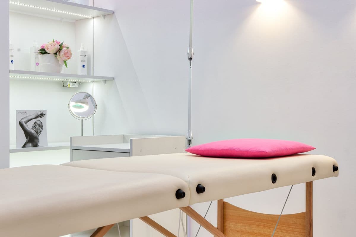 Dettaglio della sala trattamenti con lettino, mensola con prodotti professionali e fiori freschi