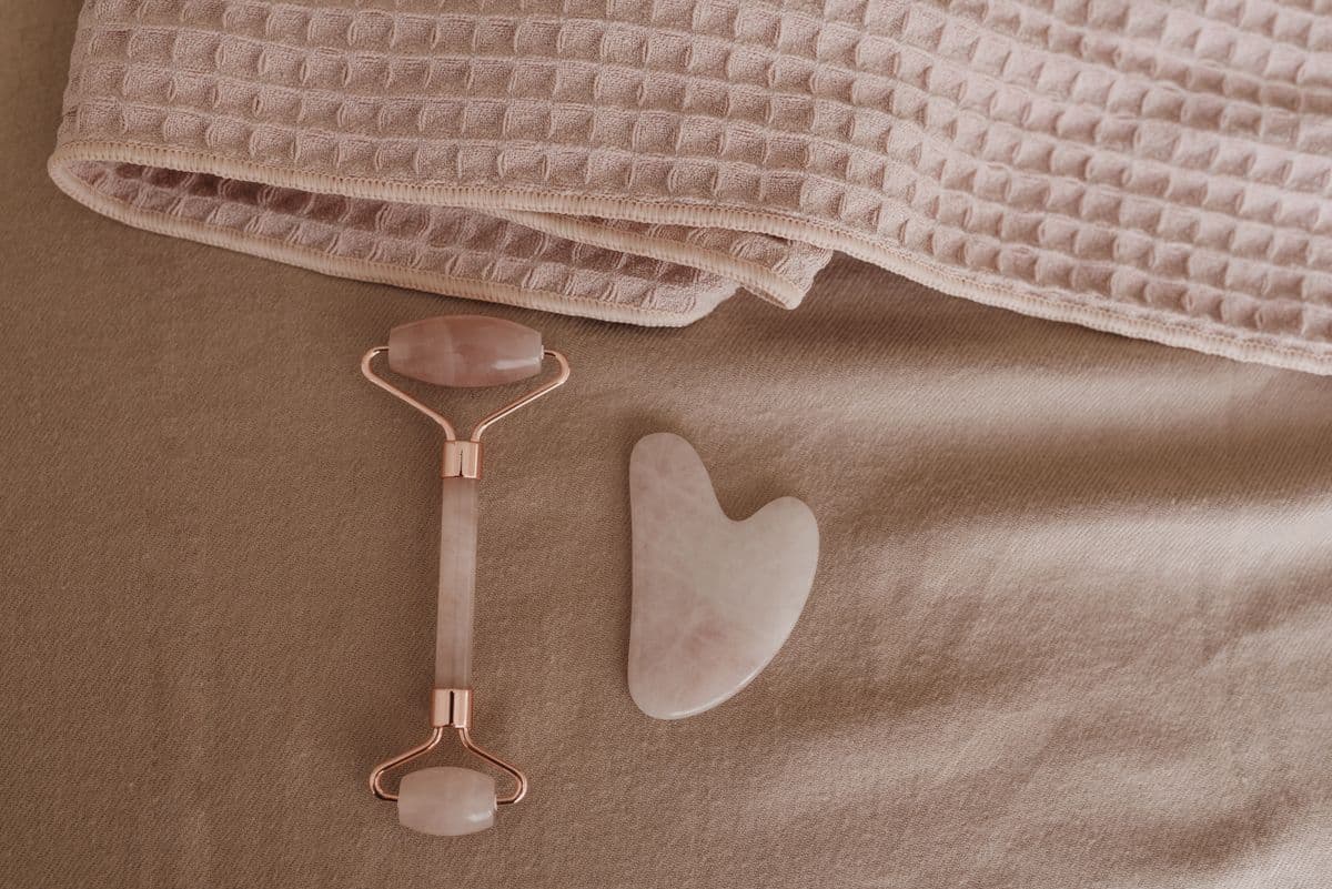 Rullo in quarzo rosa e gua sha appoggiati su un asciugamano rosa cipria