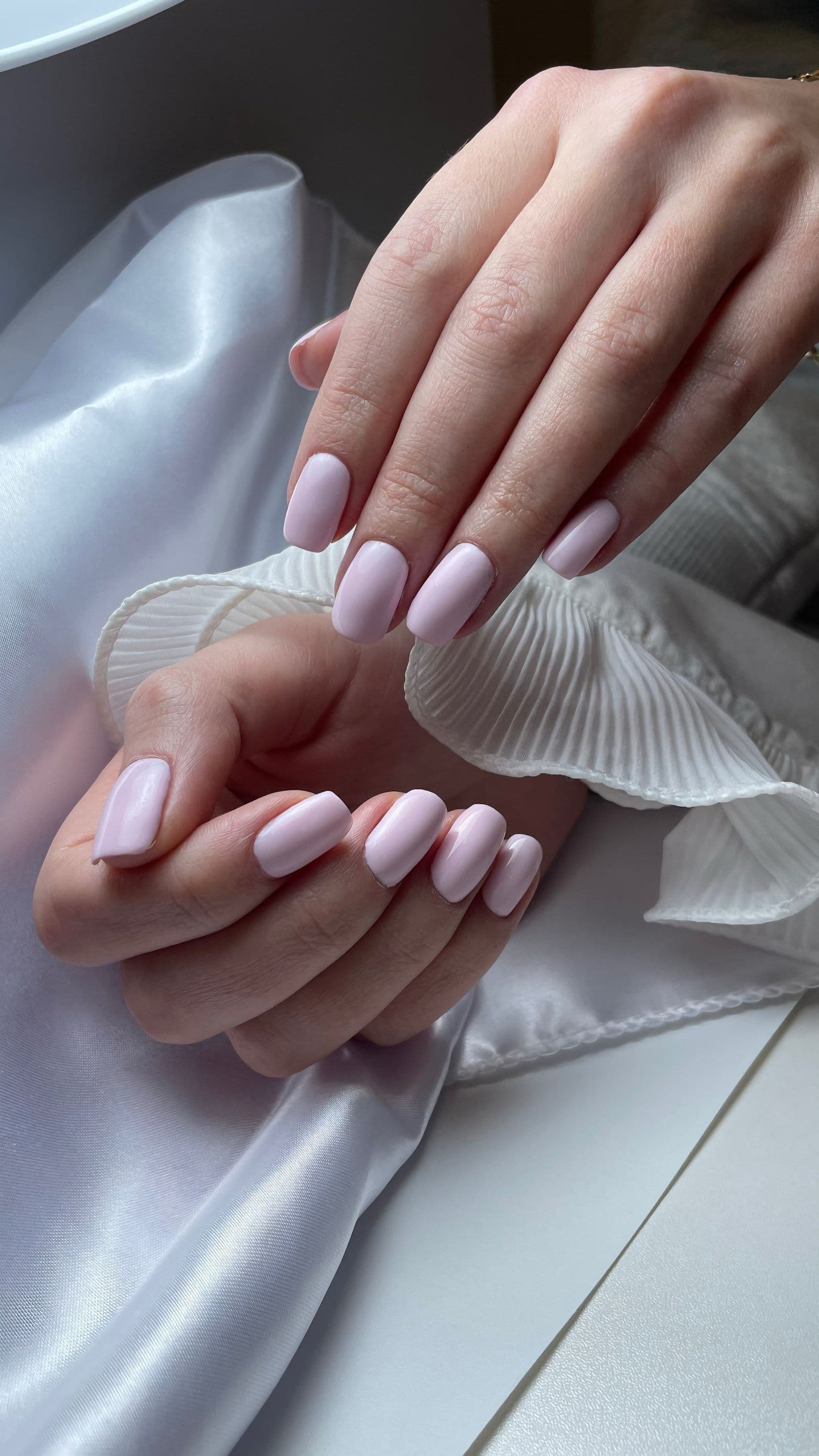 Primo piano di mani con manicure semipermanente rosa cipria appoggiate su un tessuto di raso