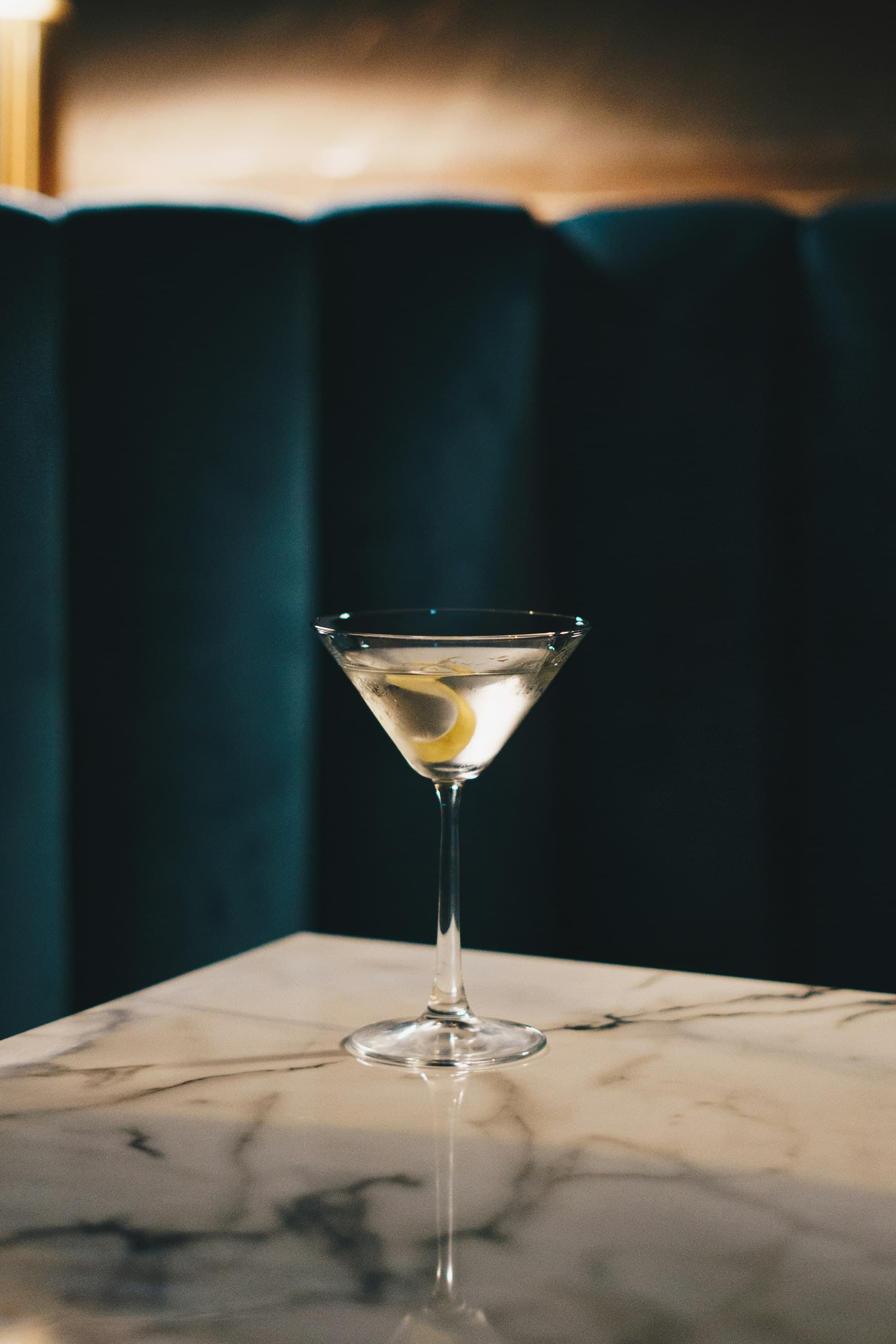 Martini limpido con scorza di limone servito su un tavolo di marmo, con boiserie verde scuro sullo sfondo