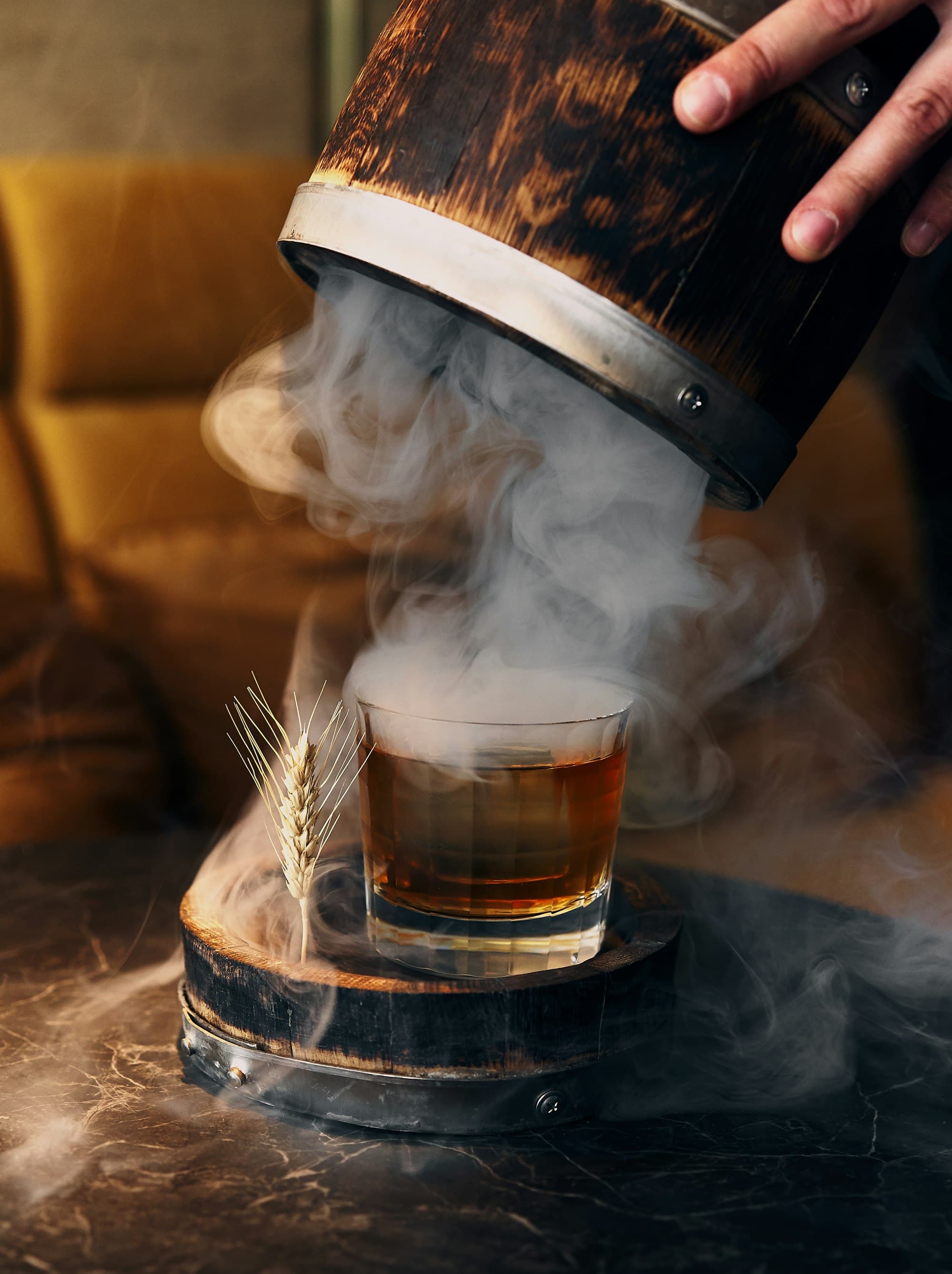 Old fashioned servito in un bicchiere basso avvolto dal fumo di legno affumicato, con spiga di grano come guarnizione