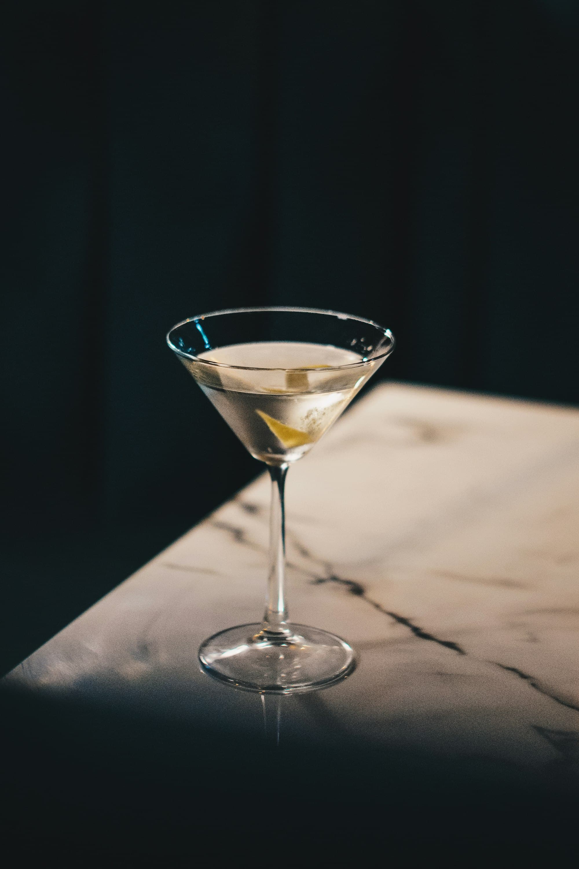 Martini con oliva servito su un tavolo di marmo bianco venato in un angolo del locale illuminato di taglio