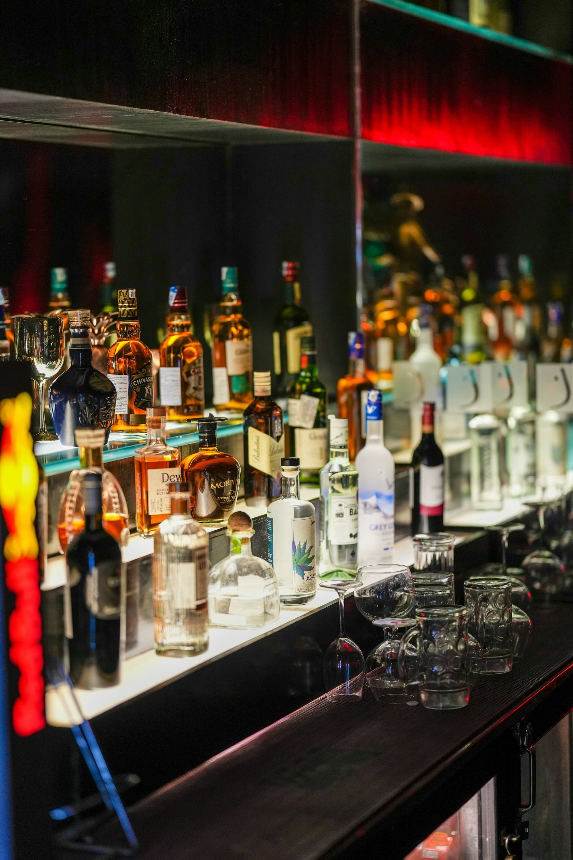 Dettaglio della parete di distillati illuminata, con etichette di gin, whisky e liquori in fila