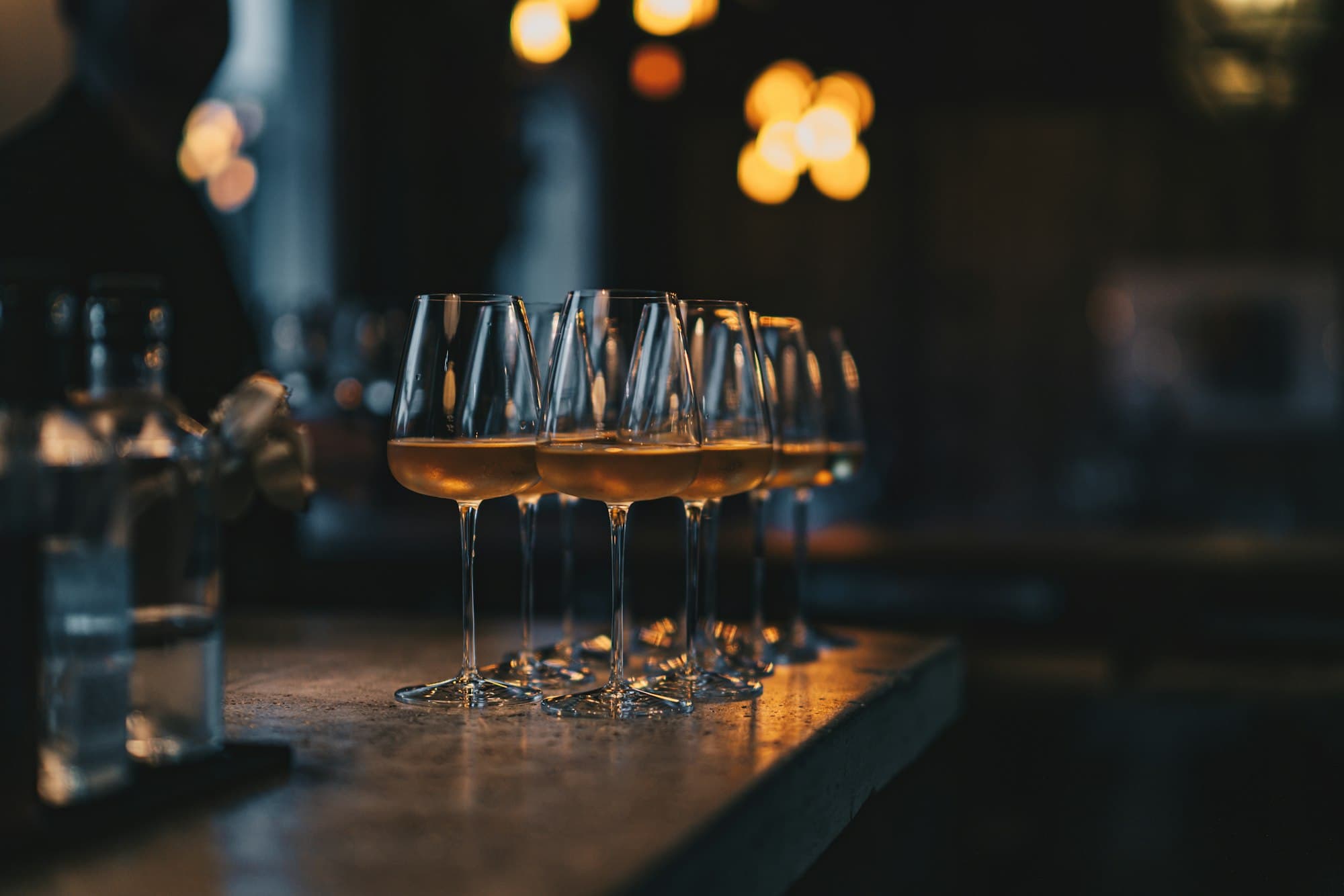 Fila di calici da aperitivo sul bancone del bar, con luci calde sfocate sullo sfondo