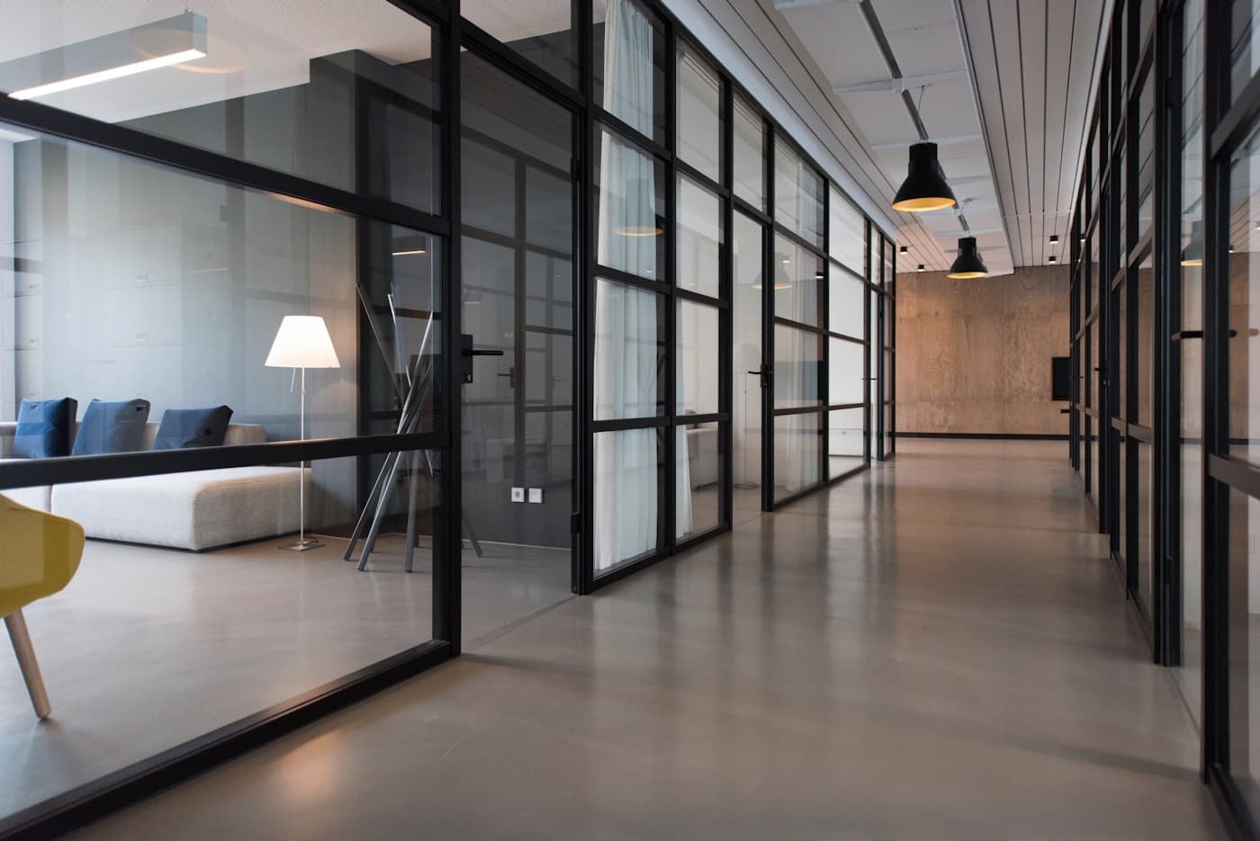 Corridoio con pareti vetrate e infissi neri che collega gli uffici open space di un progetto commerciale