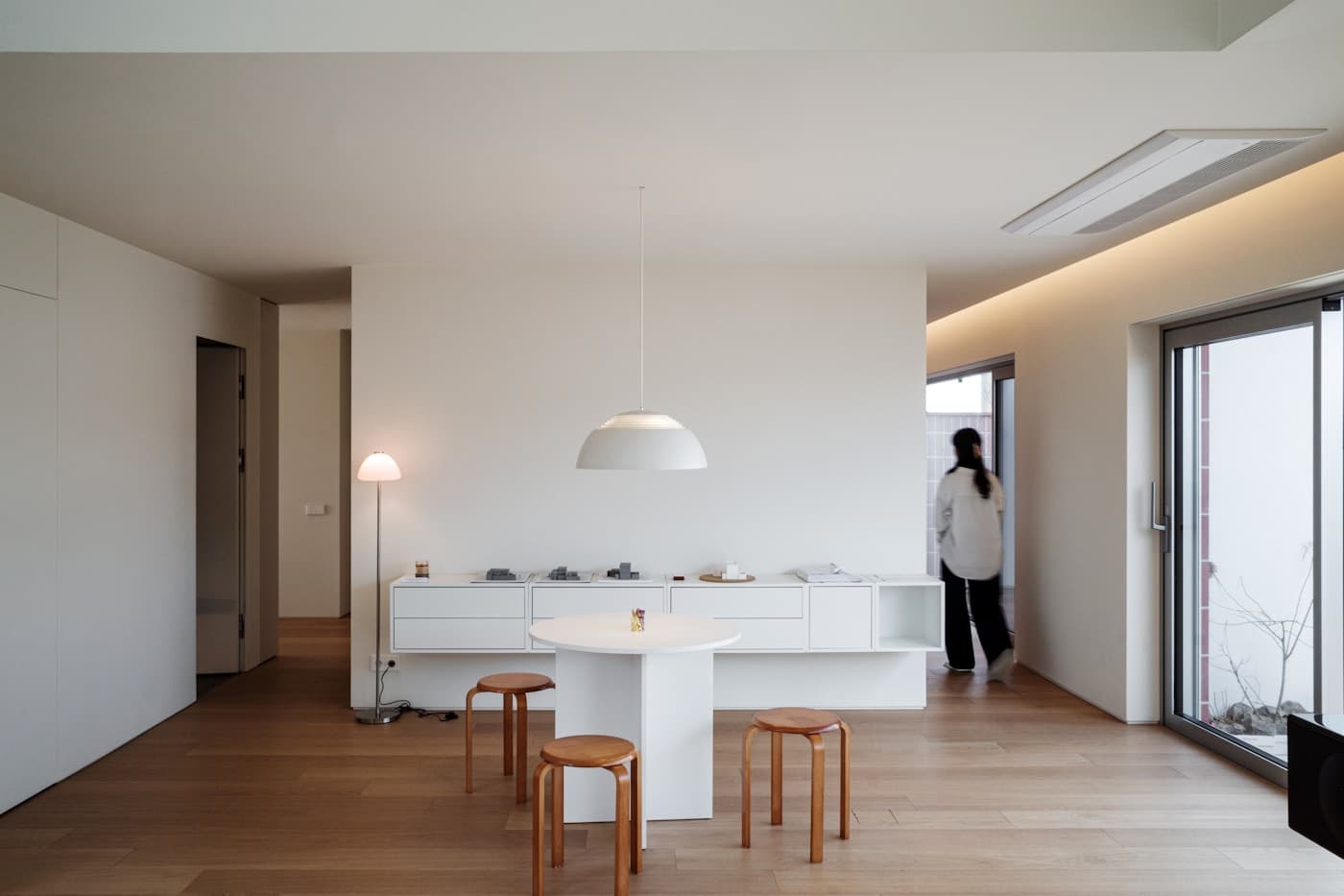 Cucina minimale bianca con isola centrale, sgabelli in legno chiaro e grandi finestre