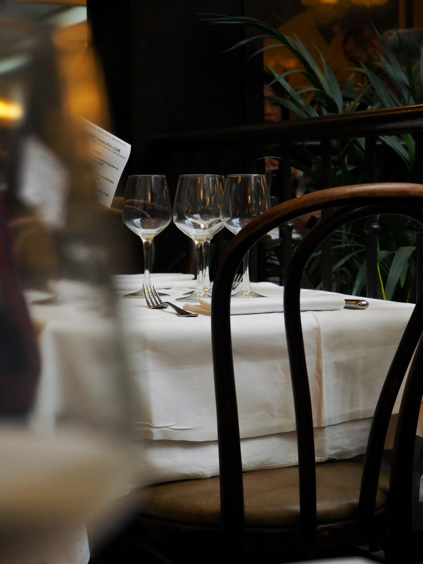 Bicchieri da vino su un tavolo apparecchiato con tovaglia bianca e piante verdi sullo sfondo