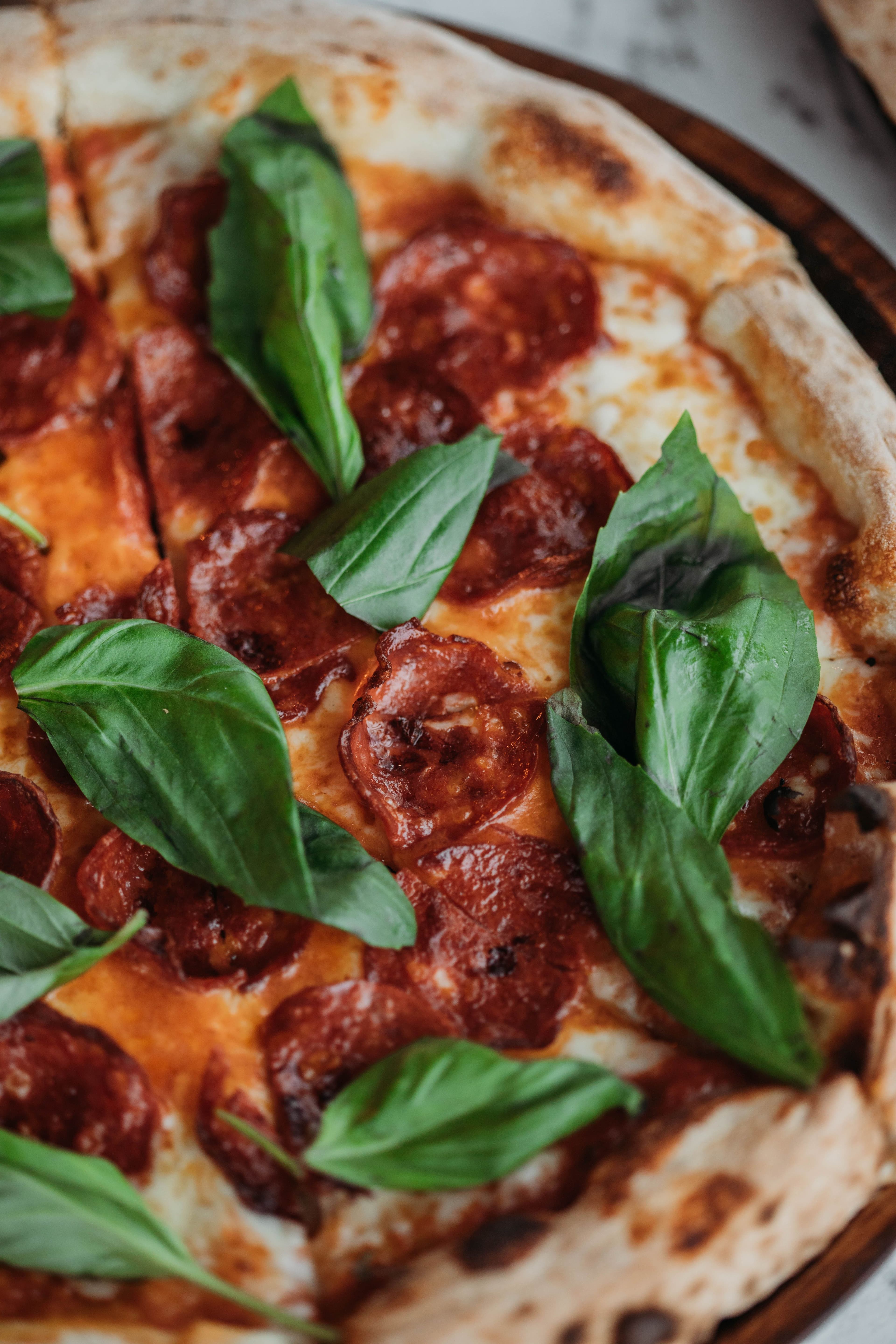 Primo piano dall'alto di una pizza al salame piccante con mozzarella filante e basilico fresco