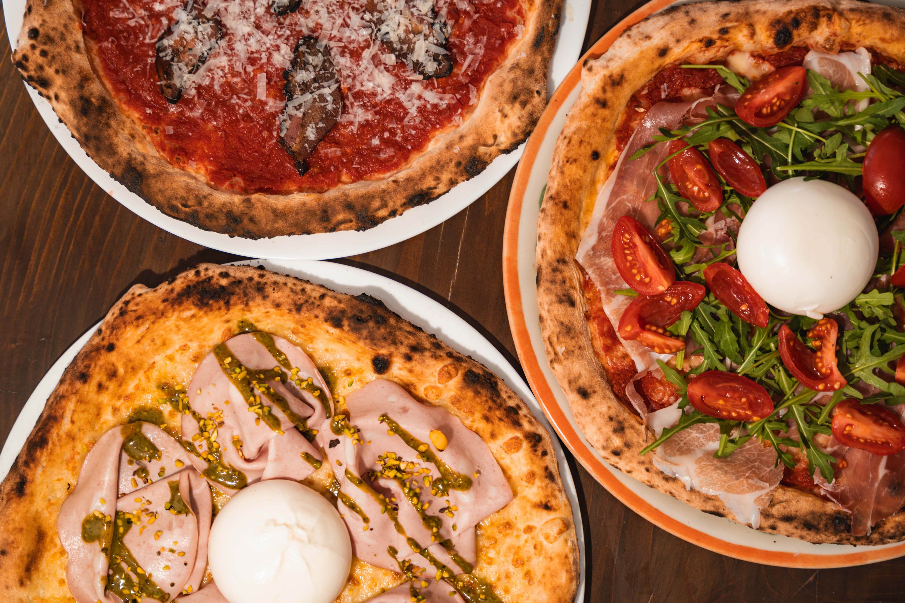 Tre pizze appena sfornate su un tavolo di legno scuro
