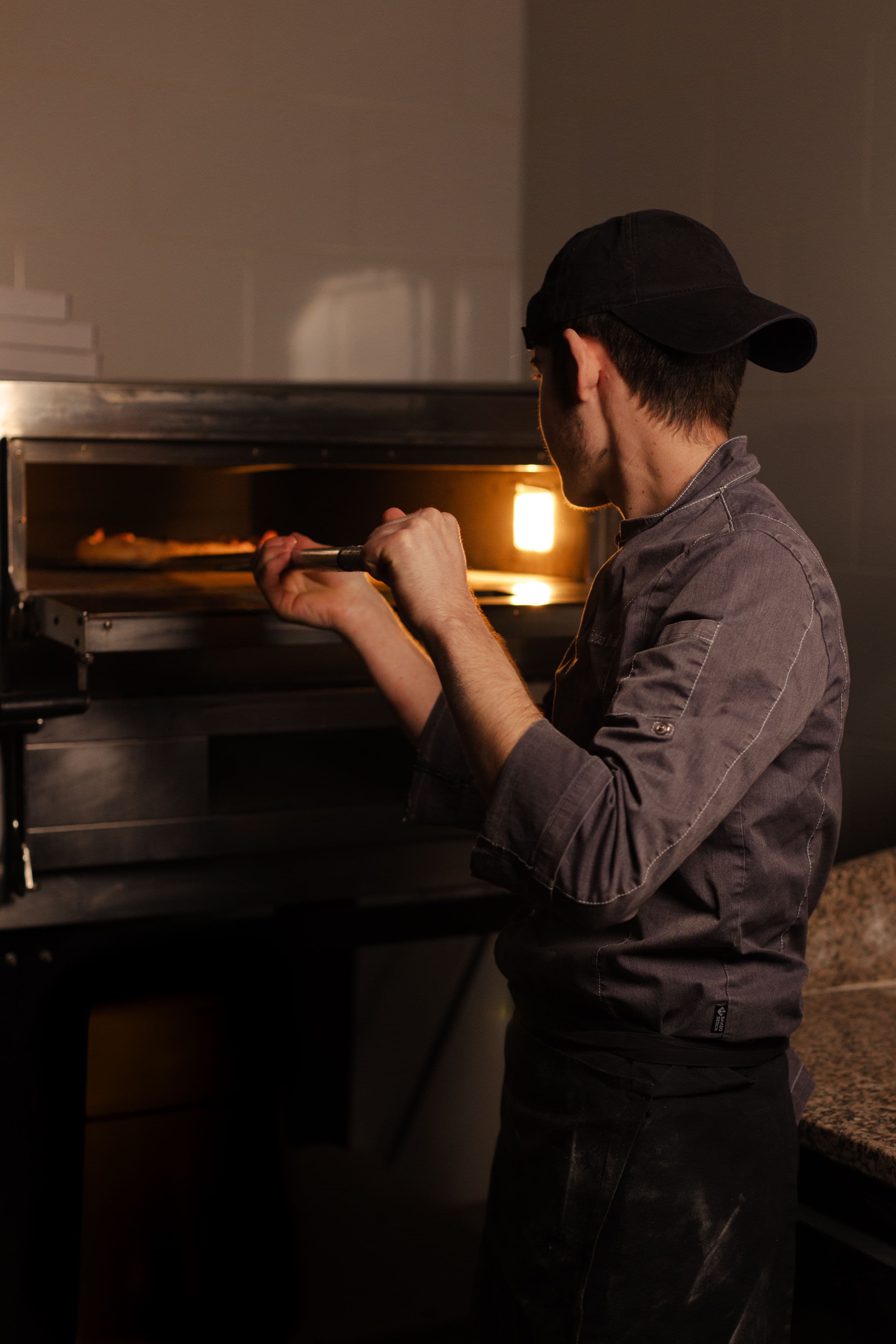 Il pizzaiolo infila una pizza nel forno a legna con la pala