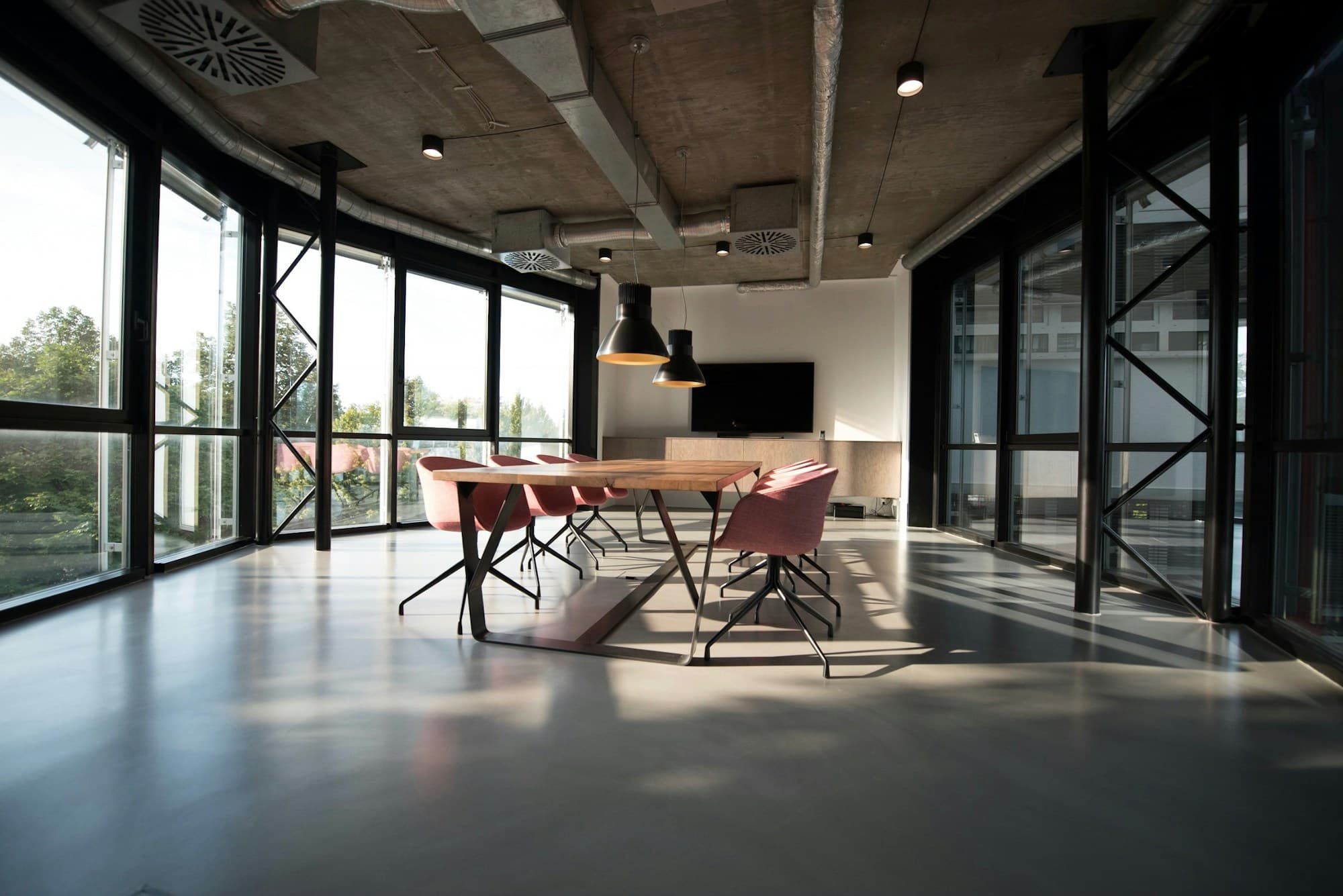 Ambiente soggiorno-pranzo minimale con grandi vetrate in ferro nero e luce naturale che attraversa lo spazio