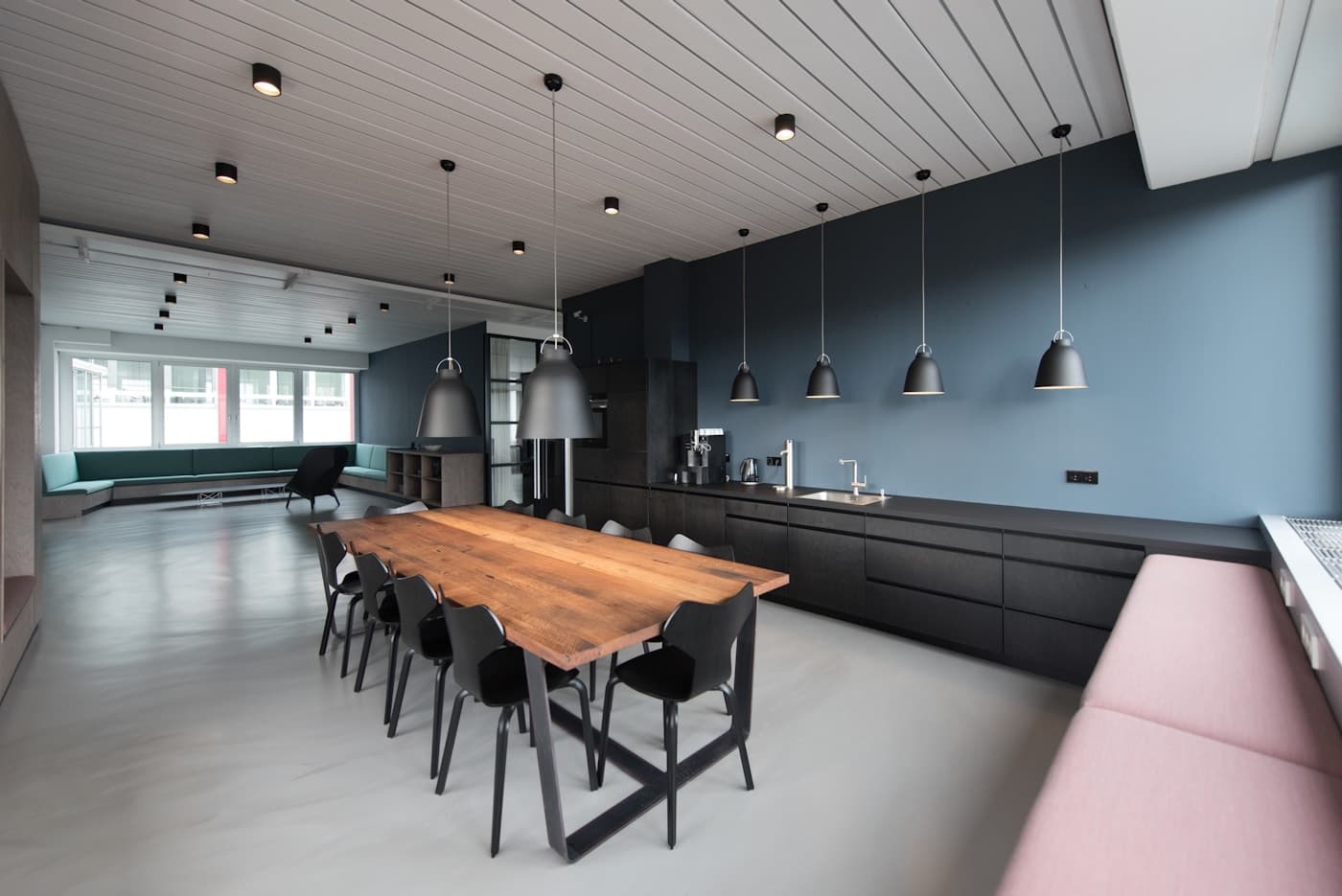 Open space con pareti blu, isola cucina in legno scuro e lampade a sospensione sopra il tavolo da pranzo