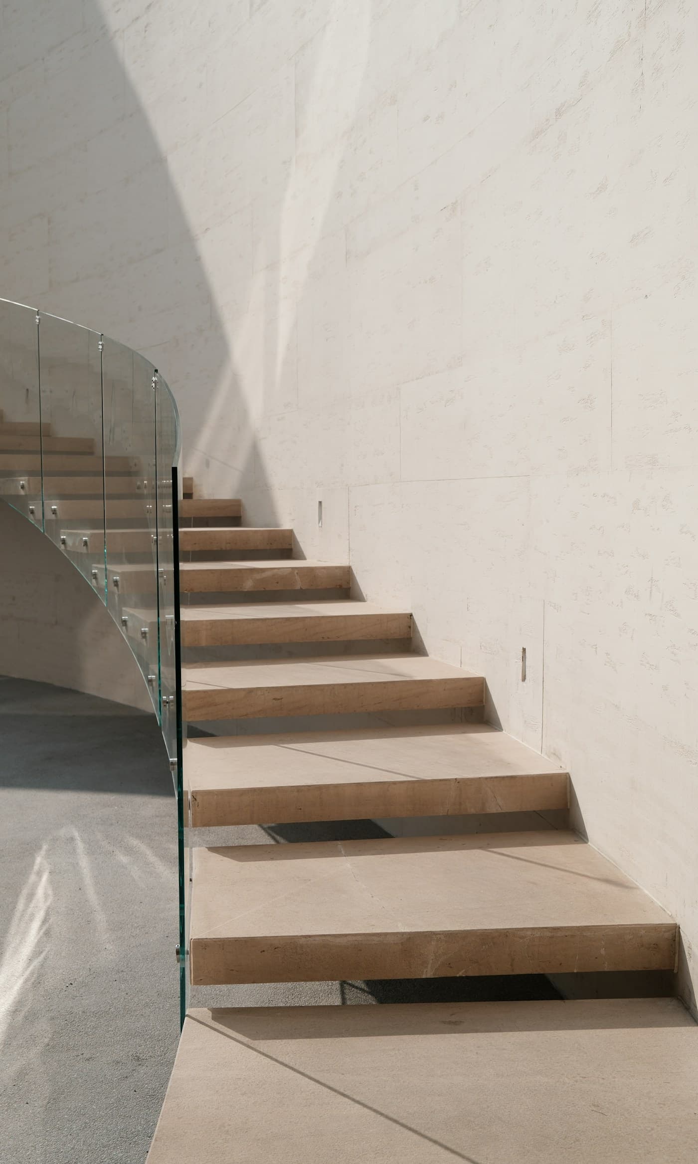 Scala in pietra sospesa con parapetto in vetro, illuminata da luce naturale radente